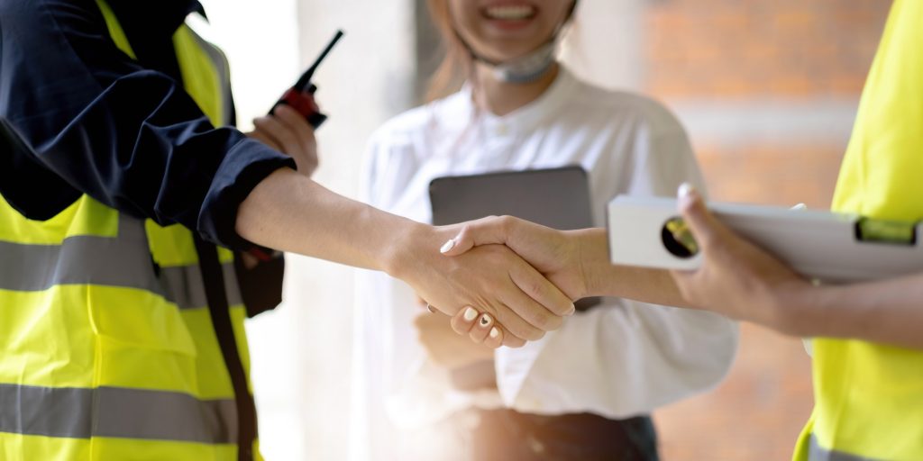 Smiling civil engineer shaking hands at construction site with businesswoman. Construction manager